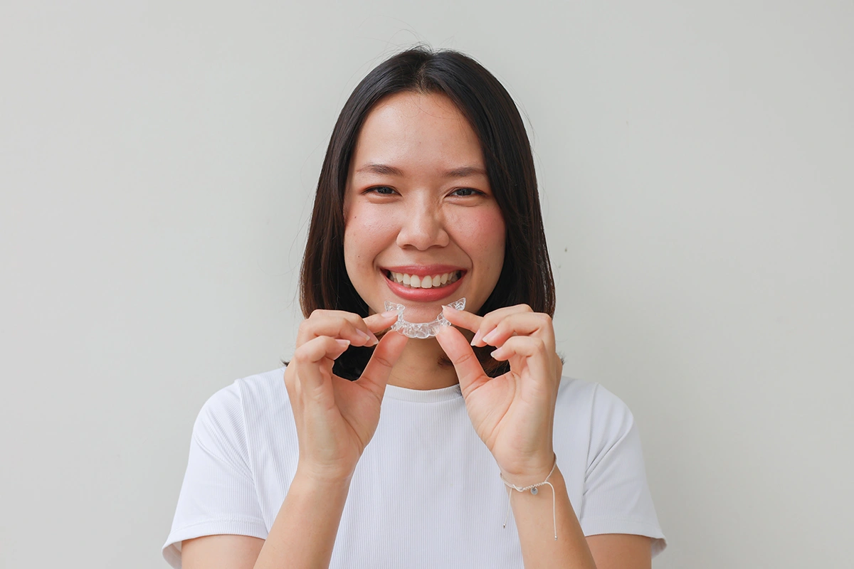 Asian lady holding a clear dental retainer and smiling.